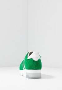 Sneaker verde in suede con accenti bianchi, forma arrotondata e suola in gomma trasparente. Presenta strisce distintive sui lati.