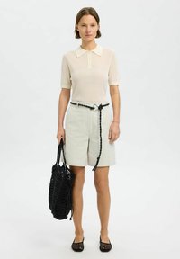 Polo en crème clair avec texture côtelée, short beige avec une ceinture tressée noire, sac fourre-tout en filet noir et ballerines en mesh noires.