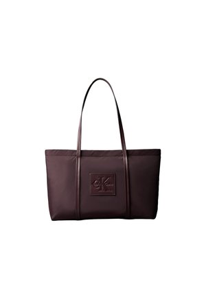 Donkerbruine rechthoekige tote bag met twee dunne handvatten en een vierkante patch met geperst "ck Calvin Klein" logo aan de voorkant.