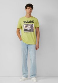 Limettengrünes Baumwoll-T-Shirt mit einem Grafikdruck eines alten Fernsehers und dem Text "Mach deine Welt GRÖßER" sowie "Discovery Channel."