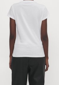 Biała koszulka z krótkim rękawem, z okrągłym dekoltem, wykonana z miękkiej bawełny. Czysty design, gładka faktura, brak widocznych wzorów lub grafik z tyłu.