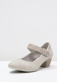 Jasnoszare zamszowe buty typu Mary Jane z teksturowanym paskiem na kostce, okrągłym noskiem i niskim, ściętym obcasem. Posiadają zapięcie na klamrę.