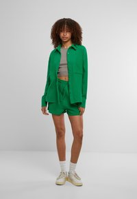 Ensemble comprenant une chemise verte et un short en tissu texturé. La chemise a une coupe décontractée avec une poche, tandis que le short possède une taille élastique.