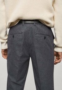 Pantaloni grigi realizzati in tessuto testurizzato con tasche laterali, dettagli in bottone e un design aderente, indossati con un maglione crema.