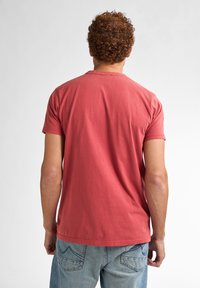 Camiseta de algodón roja con mangas cortas, escote redondo y un corte relajado, combinada con unos jeans de mezclilla azul claro que tienen bolsillos traseros cosidos.