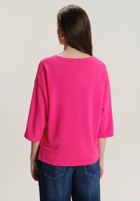 Jasnoróżowa, żeberkowana bluzka z szerokim dekoltem, rękawami 3/4 i bocznymi rozcięciami, w połączeniu z niebieskimi dżinsami. Gładka faktura, casualowy design.