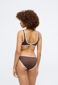 Brown ribbed bikini set with white accents. The top has wide straps and a rear clasp, while the bottoms are high-waisted with white trim.