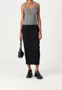Šedý žebrovaný top bez rukávů, černá džínová sukně střední délky s knoflíkovými detaily, černé robustní mokasíny a malá černá kabelka.