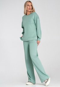 Miętowy sweter i dopasowane szerokie spodnie, wykonane z miękkiego materiału w luźnym fasonie. Posiada długie rękawy i okrągły dekolt.