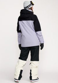 Ski jakke i lys lavendel og sort, med h�ætte, parret med sorte og cremefarvede skibukser. Har en afslappet pasform og funktionelt design.