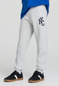 Jasnoszare dresy o luźnym kroju, z ciemnogranatowym nadrukiem "NYC" na lewej udzie i ściągaczami. W połączeniu z czarnymi trampkami.