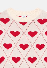 Pleteni pulover s kremno osnovo in diamantnim vzorcem z rdečimi srci, rebrastim izrezom in teksturirano površino.