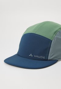 Boné bicolor com painéis verde e azul, feito de tecido leve. Inclui uma pala azul e o logótipo bordado "Vaude".