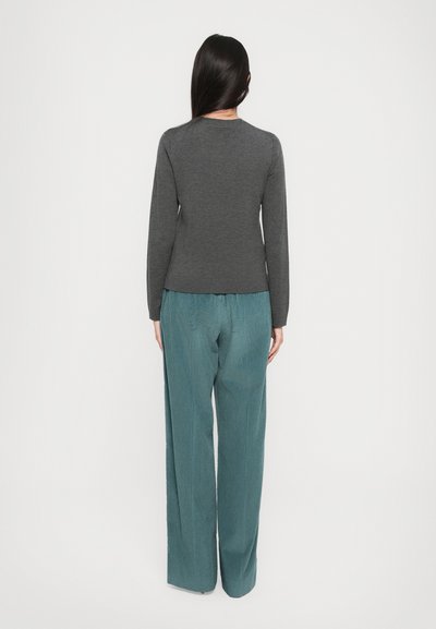 Pulover gri cu mâneci lungi și decolteu în formă de cerc, asortat cu pantaloni largi de culoare teal, cu textură ribbed verticală. Ambele articole au o croială lejeră.
