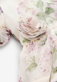 Cvetlična prosojna tkanina s svetlo rožnatimi in zelenimi odtenki, okrašena z vrtečo se tkaninsko rožo za dodaten detajl.