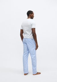 Vaaleanharmaa lyhythihainen paita yhdistettynä sinivalkoraidallisiin pyjamahousuihin. Housuissa on joustava vyötärönauha ja rento istuvuus.