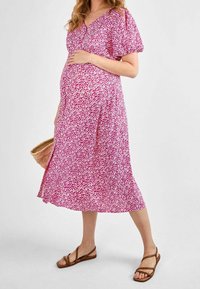 Rosa blumenmuster Schwangerschafts Kleid mit kurzen Puffärmeln, V-Ausschnitt, fließendem Saum und leichtem Material, kombiniert mit braunen Sandalen mit Riemen und einer geflochtenen Tasche.