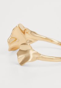 Anillo de color dorado con un acabado suave y pulido, que presenta un diseño que recuerda a dos pétalos florales en los extremos, con forma curvada y asimétrica.