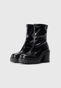 Bottines noires avec une finition brillante, panneaux latéraux élastiques, semelle à plateforme épaisse et talon carré. Semelle en caoutchouc texturé pour une meilleure adhérence.