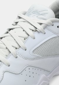 Weißer Sportschuh mit strukturierten Schnürsenkeln, perforiertem Leder, Netzseitenpanel und gepolsterter Zunge mit dezentem, eingeprägtem Logo.