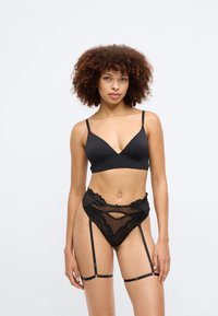 Ensemble de lingerie noire comprenant un bralet lisse avec de fines bretelles et un shorty en dentelle transparente avec des pois et des porte-jarretelles.
