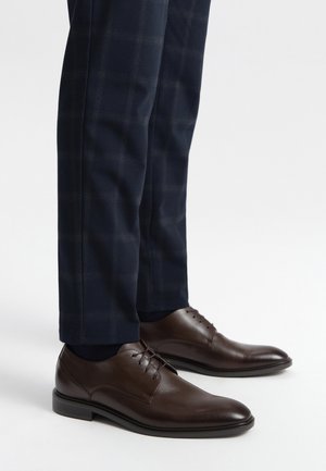 Zapatos de vestir de cuero marrón con un acabado suave y cordones, combinados con pantalones a rayas de cuadros azul oscuro que presentan un sutil patrón de cuadros.