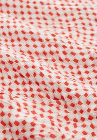 Tissu en coton présentant un fond blanc avec un motif de losanges rouges répété. La texture semble froissée et légère.