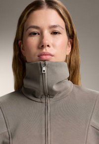 Szürke, magas nyakú dzseki, cipzárral, texturált anyagból. Függőleges varrásokkal és testhezálló szabással rendelkezik.