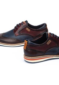 Chaussures en cuir présentant une combinaison de panneaux marron foncé et bleu marine, des perforations décoratives et une semelle rayée multicolore.