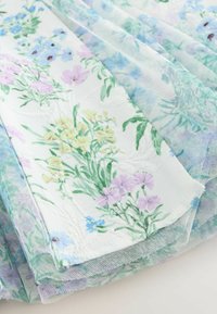 Tessuto bianco con stampe floreali pastello in giallo, viola e blu, sovrapposto a un tulle floreale trasparente blu-verde.