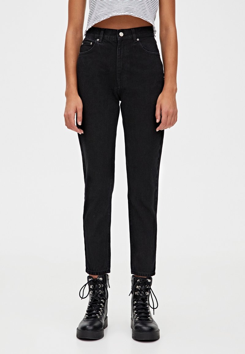 Zwarte denim jeans met hoge taille en een aansluitende pasvorm, met rechte pijpen, voorzakken en een rauwe zoom, gecombineerd met zwarte veterschoenen.