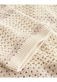 Gestrickte Decke in Creme und Beige mit einem offenen Gewebe-Design und einem strukturierten Muster. Die Kanten haben einen gerippten Abschluss.