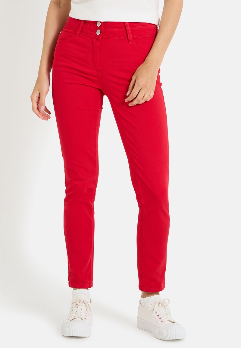 Pantalones ajustados rojos, fabricados en una tela elástica, que presentan dos bolsillos frontales y botones metálicos en la cintura, combinados con zapatillas blancas.