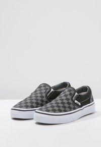 Scarpe slip-on a scacchi neri e grigi con accenti elastici laterali, suole in gomma bianca e dettagli di cucitura a contrasto.