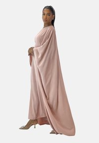Long pink dress with wide sleeves and a flowing design. The fabric appears soft and lightweight, complemented by transparent heeled shoes.