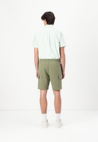 Lysegrønn kortermet skjorte med plissee bak, kombinert med olivenfargede cargo-shorts med to sidelommer, stylet med hvite joggesko.
