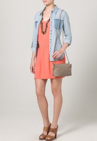 Vestido de color coral con cintura fruncida, camisa de mezclilla superpuesta, un bolso cruzado beige y sandalias de plataforma marrones.