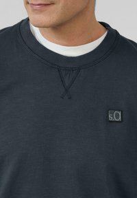 Donkerblauwe katoenen sweatshirt met een ronde kraag, gestructureerde stiksels en een klein rechthoekig logopatch op de borst.