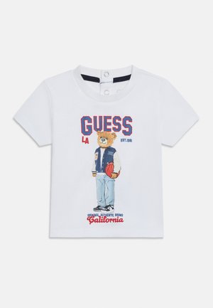T-shirt blanc à manches courtes pour tout-petit avec un ours portant une veste universitaire et tenant un ballon de basket, avec les inscriptions « GUESS », « California » et d'autres textes.