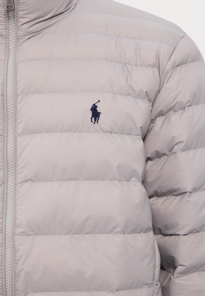 Svetlosivá prešívaná bunda s horizontálnym prešívaním, zapínanie na zips a vyšitým námorníckym logom na hrudi. Hladká textura.