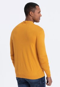 Men's long-sleeve sweater in bright mustard. Textured knit, crew neck, and ribbed cuffs. Paired with dark denim jeans.
