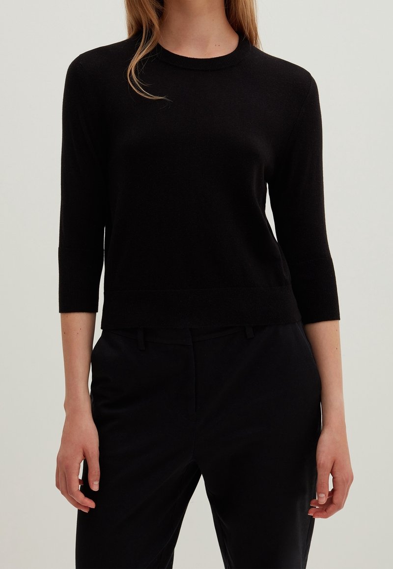 Černý přiléhavý svetr s tříčtvrtečními rukávy, kulatým výstřihem a žebrovanými detaily na lemu a manžetách, vyrobený z měkkého materiálu.