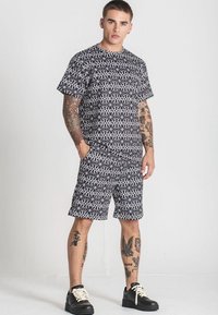 Čiernobiely krátky rukáv tričko a šortky set. Obsahuje geometrický dizajn, voľný strih a okrúhly výstrih. Ozdobené tetovaním.