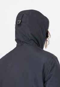 Svart vattentät jacka med huva, med en texturerad utsida och justerbara remmar. Bakvy visar dess minimalistiska design och silhuett.