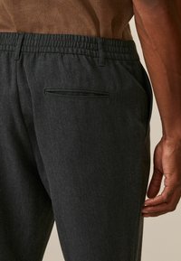Pantalons stretch gris pour homme avec une taille plate, des poches latérales et arrière, et une texture douce, mettant en avant un design soigné.