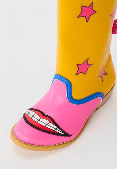 Bright yellow and pink cowboy boot with red star patterns on the shaft and a cartoon-style mouth graphic on the toe.