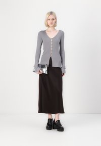 Gray ribbed cardigan with buttons, paired with a brown satin midi skirt. Model holds a metallic silver clutch and wears black platform shoes.