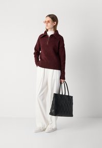 Bordeaux zip-kraagtrui, witte hoge taille broek en een zwarte geweven leren tote bag met dubbele handvatten, gecombineerd met witte sneakers.