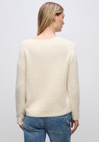 Cremefarbener Pullover aus weichem, strukturiertem Stoff mit langen Ärmeln und rundem Hals; kombiniert mit Denim-Jeans.