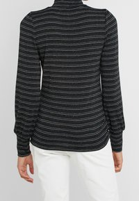 Haut à manches longues à rayures noires avec un col montant, présentant des fils métalliques multicolores, un tissu texturé et des manches froncées aux poignets.